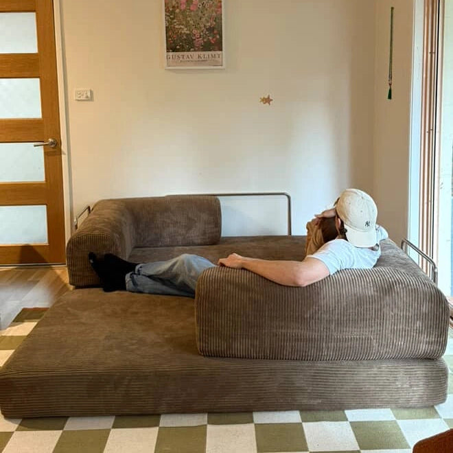 Person lying on a coffee sofa in a room with a checkered floor and a door in the background.